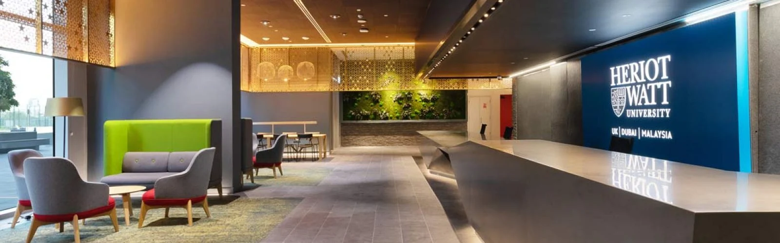 Modern reception lounge at Heriot-Watt University Dubai campus featuring a sleek marble-style desk, colourful seating pods, and the illuminated university logo.